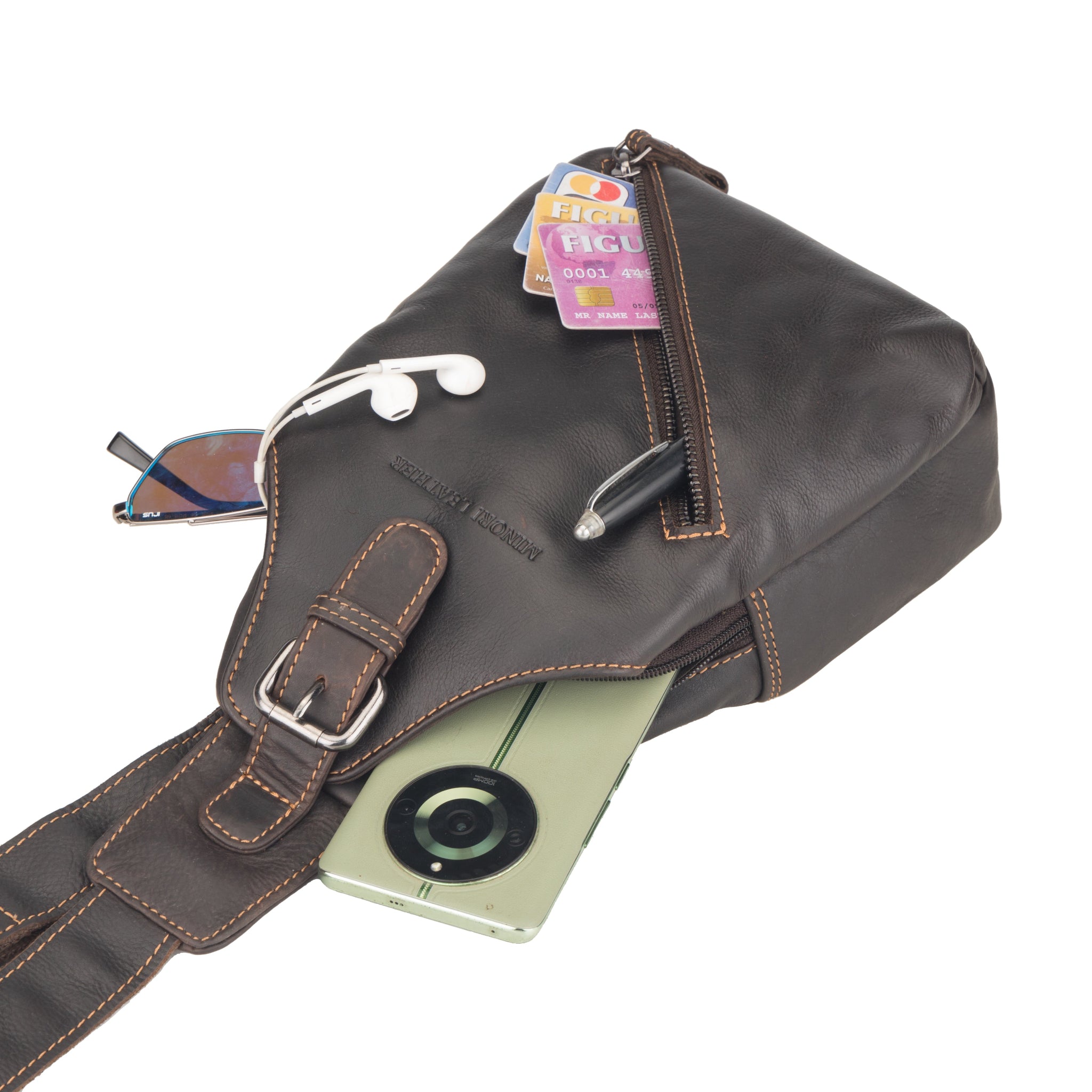Brown Minori leather sling bag with everyday essentials including phone, sunglasses, pen, and cards partially visible inside.