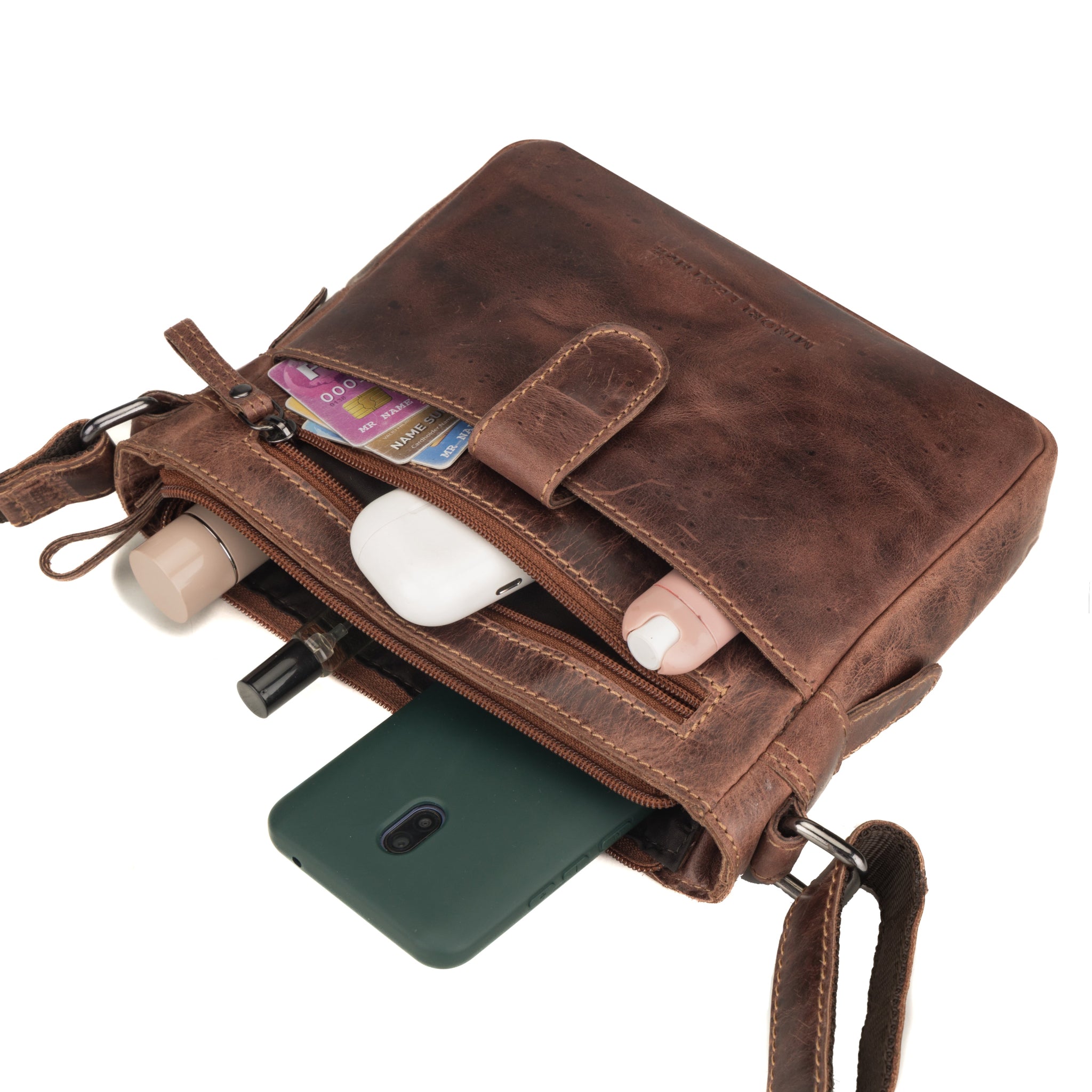 Brown Minori leather crossbody bag with compartments holding a phone, wallet, and other items on a white background