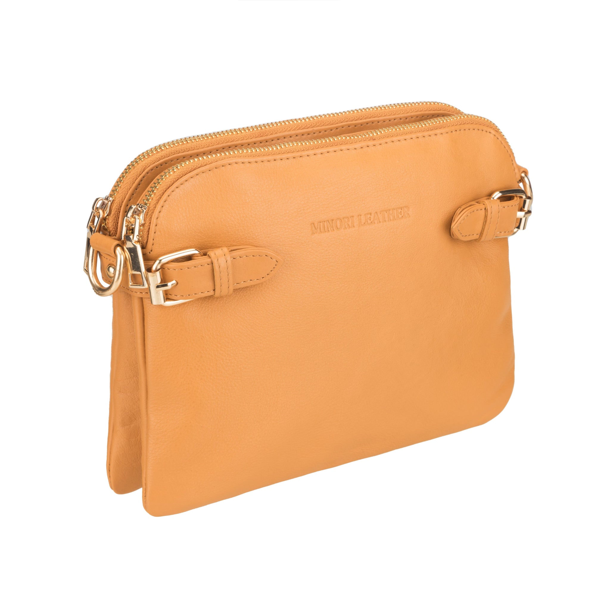 Angled view of tan Minori leather handbag showing dual zippered compartments and side buckles.