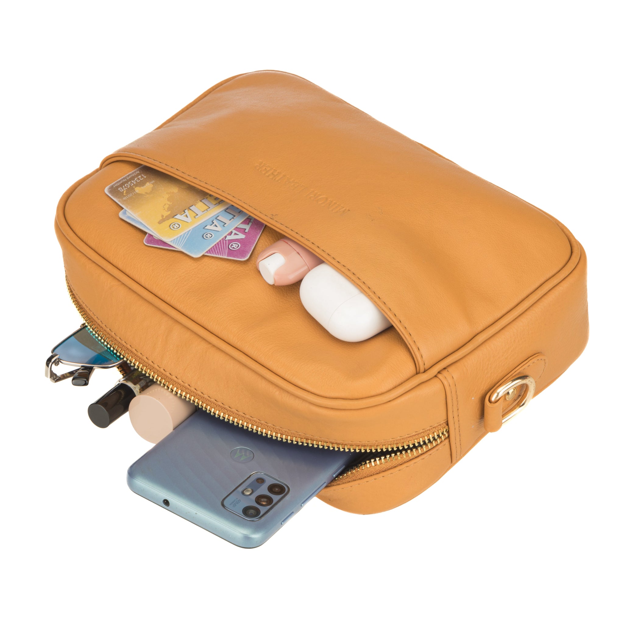 Tan Minori leather crossbody bag shown partially open and filled with daily essentials like cards, makeup, sunglasses, and a smartphone.