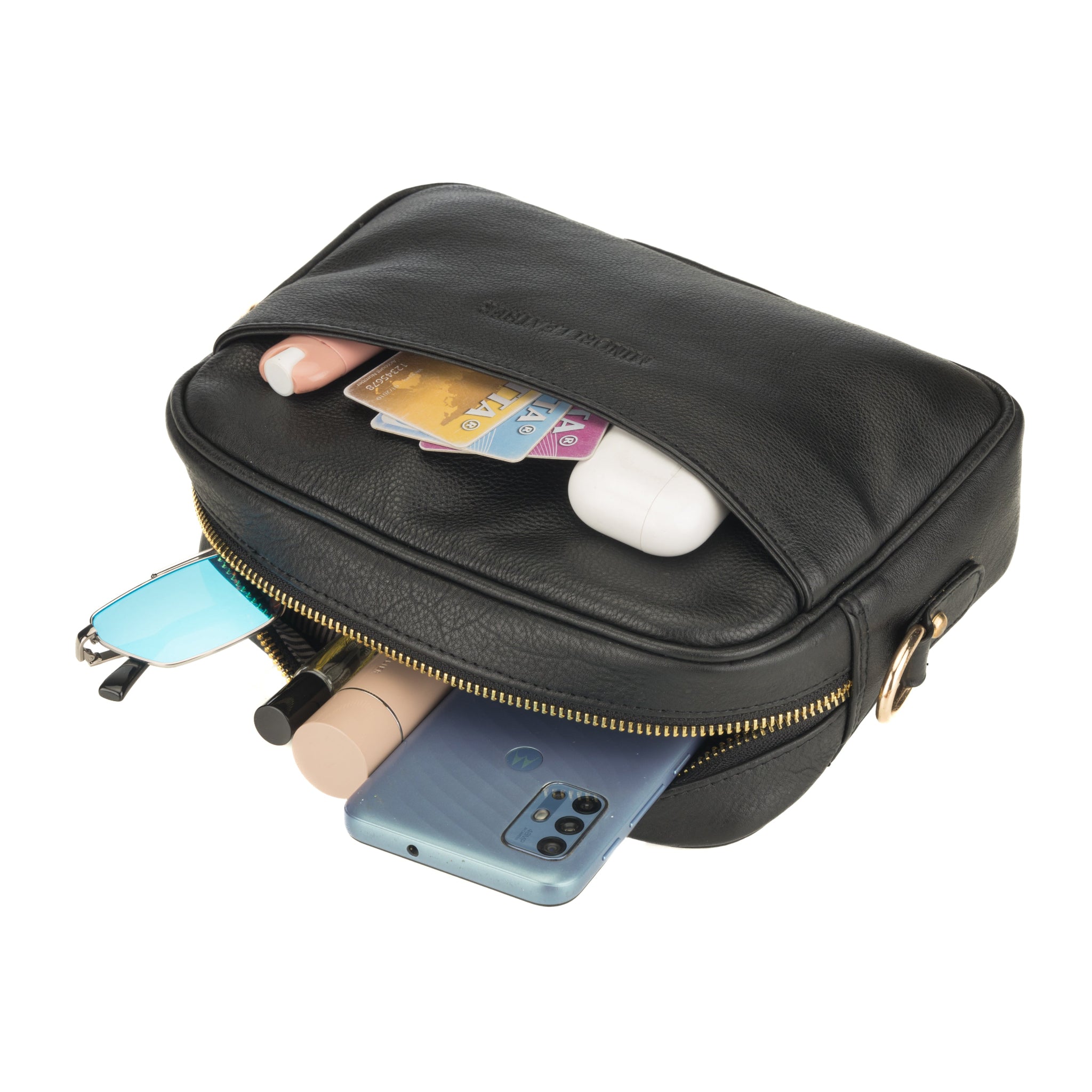 Black Minori leather crossbody bag opened and filled with everyday essentials including a phone, cards, makeup items, and sunglasses.