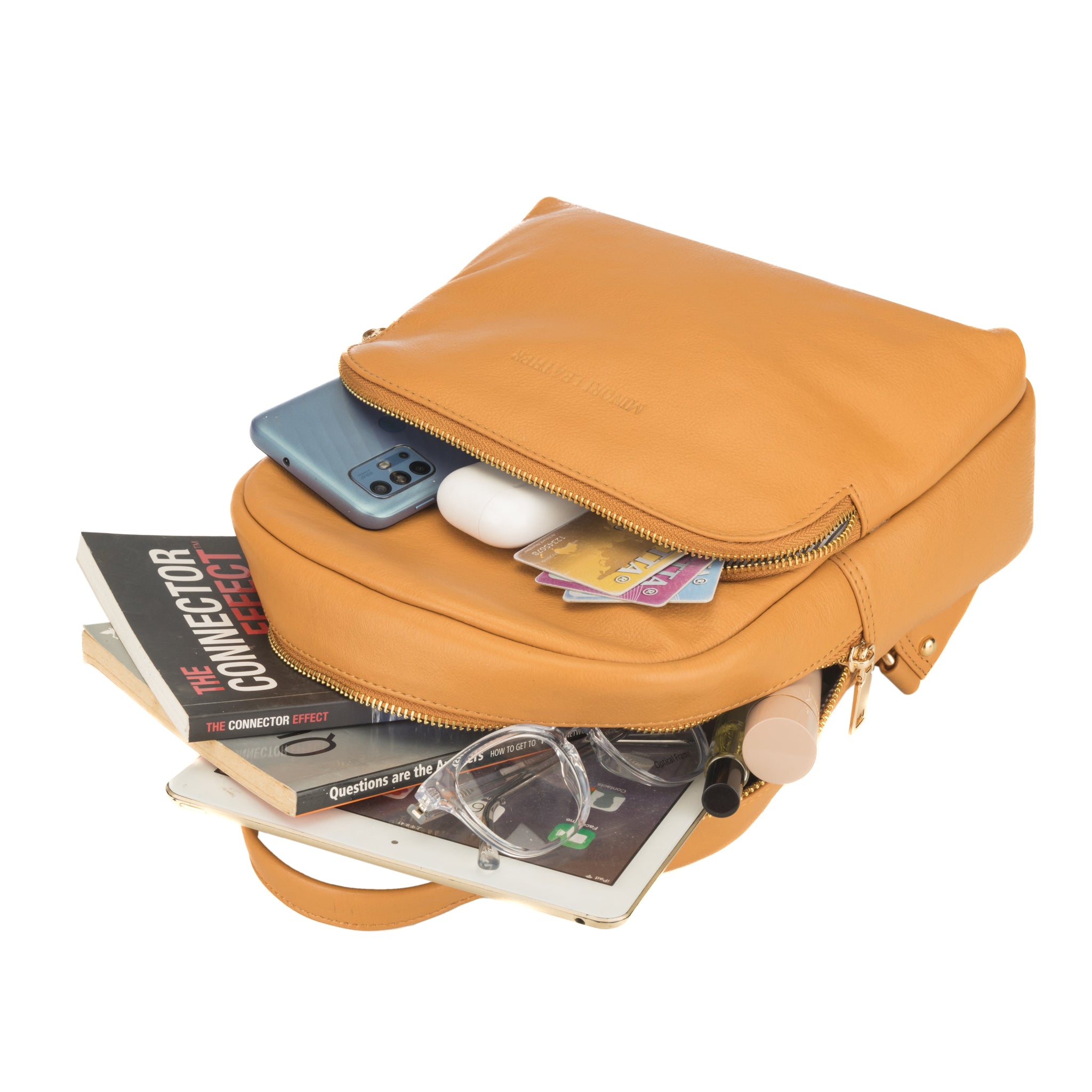 Tan Minori leather backpack with items like a phone, mouse, books, and glasses inside on a white background