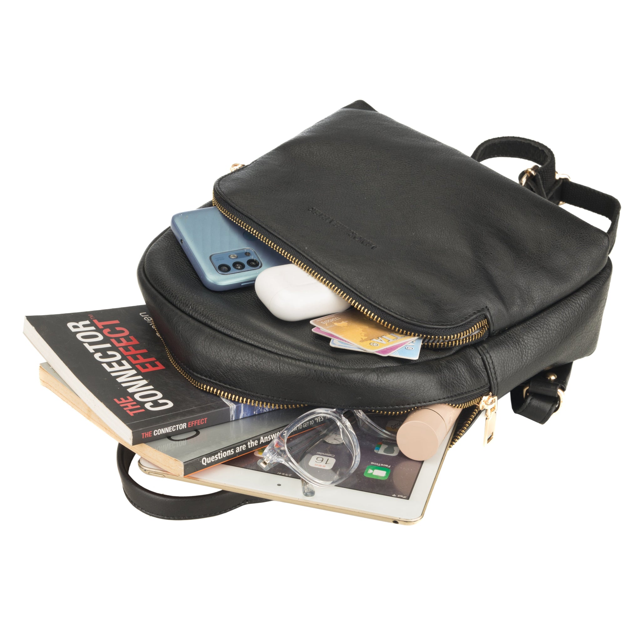 Black Minori leather backpack with items like a phone, magazine, and books on a white background