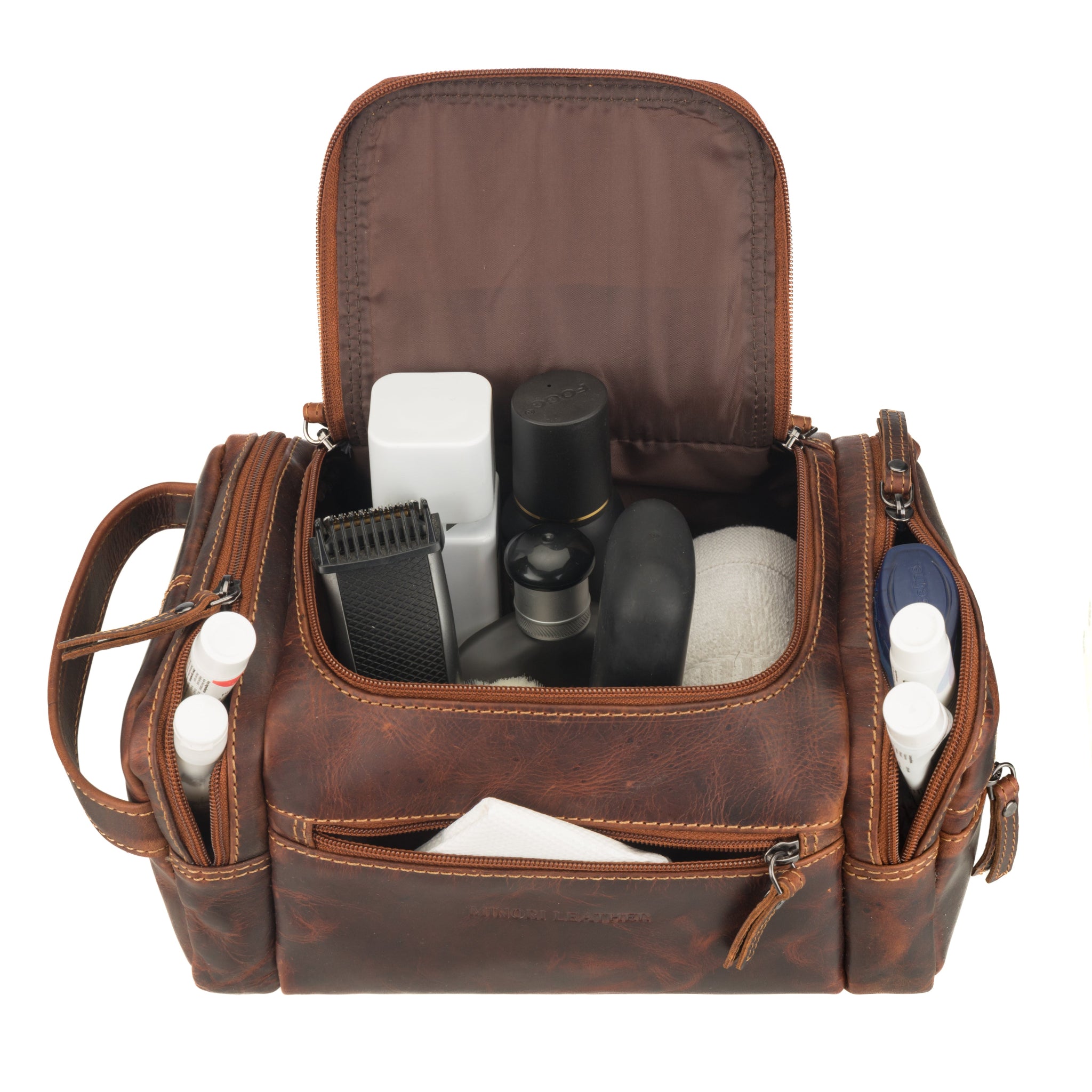 Chestnut brown Minori leather toiletry bag filled with grooming essentials such as bottles, trimmer, and travel toiletries, showing organized interior capacity.
