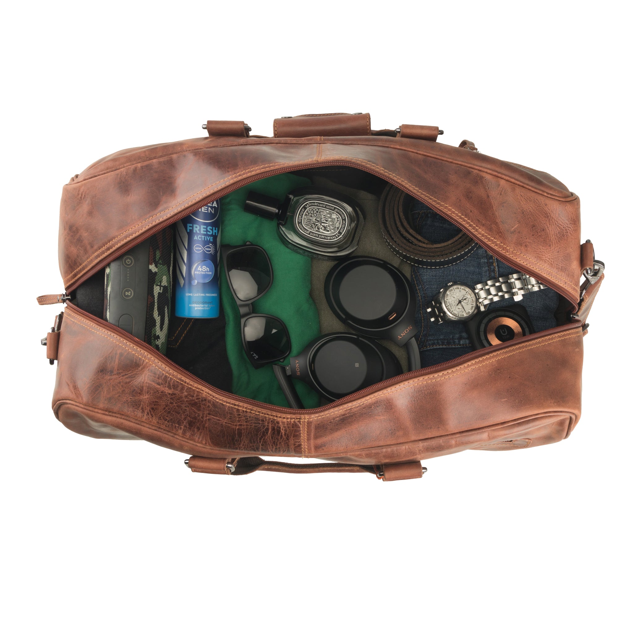 Top-down view of a chestnut brown Minori leather duffel bag fully packed with travel essentials including headphones, sunglasses, a watch, clothing, and grooming items.