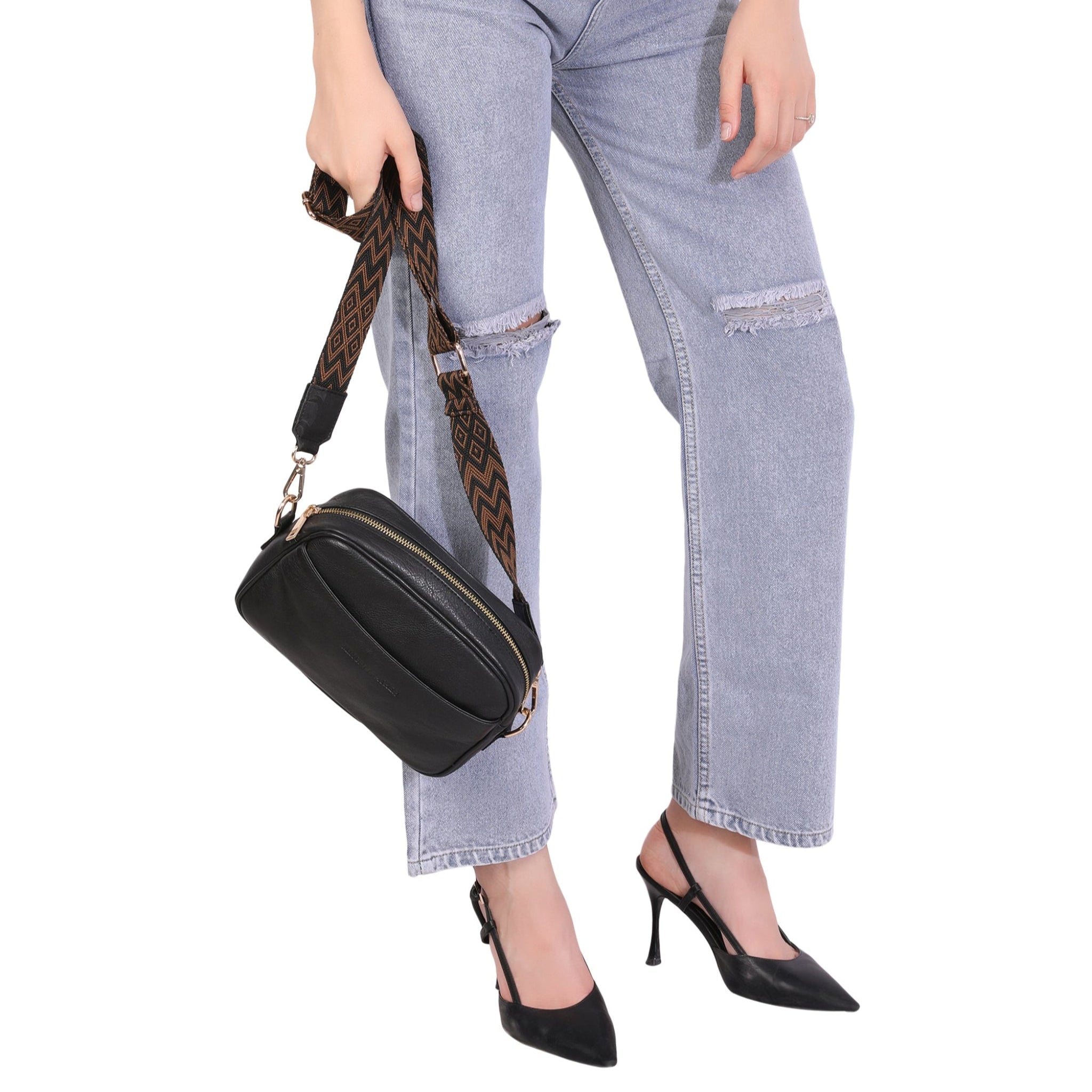 Woman modeling a black Minori leather crossbody bag with a patterned strap holding in one hand.