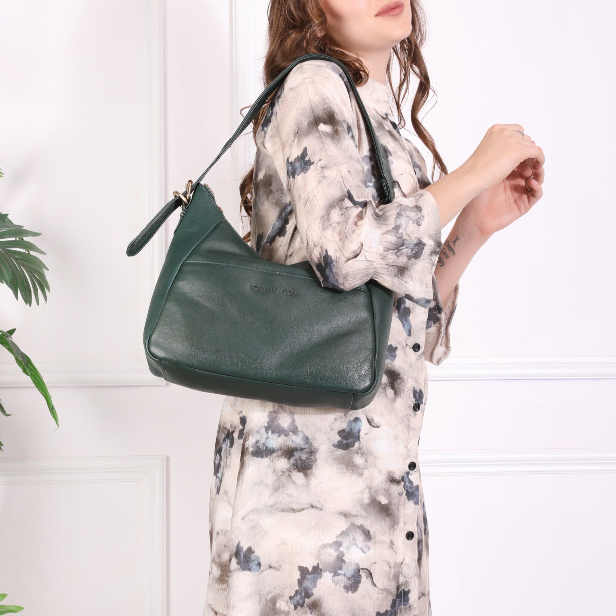 Woman wearing a floral dress and carrying a Forest Green Minori leather shoulder bag under her arm, slightly turned with a confident pose.