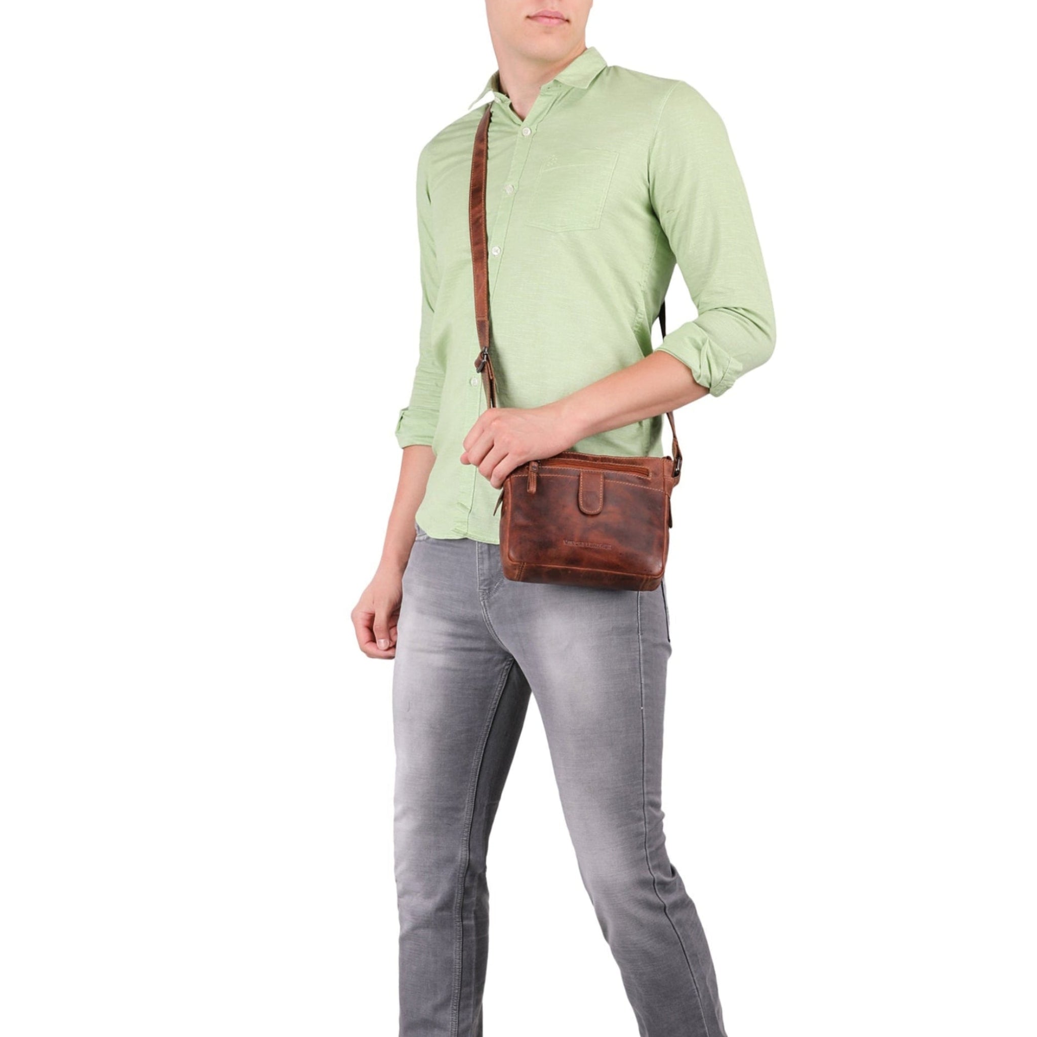 Person wearing a green shirt and gray pants with a brown Minori leather crossbody bag on a white background
