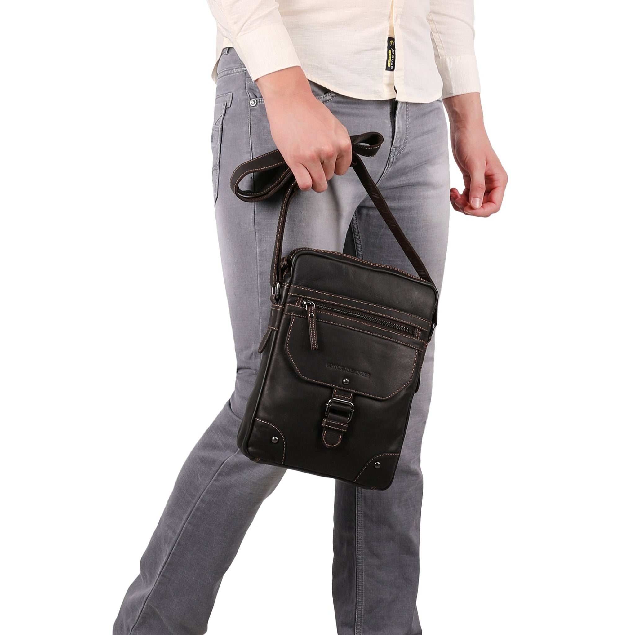 Brown Minori leather crossbody bag held by the strap at waist level, emphasizing the bag’s portability and rugged design.