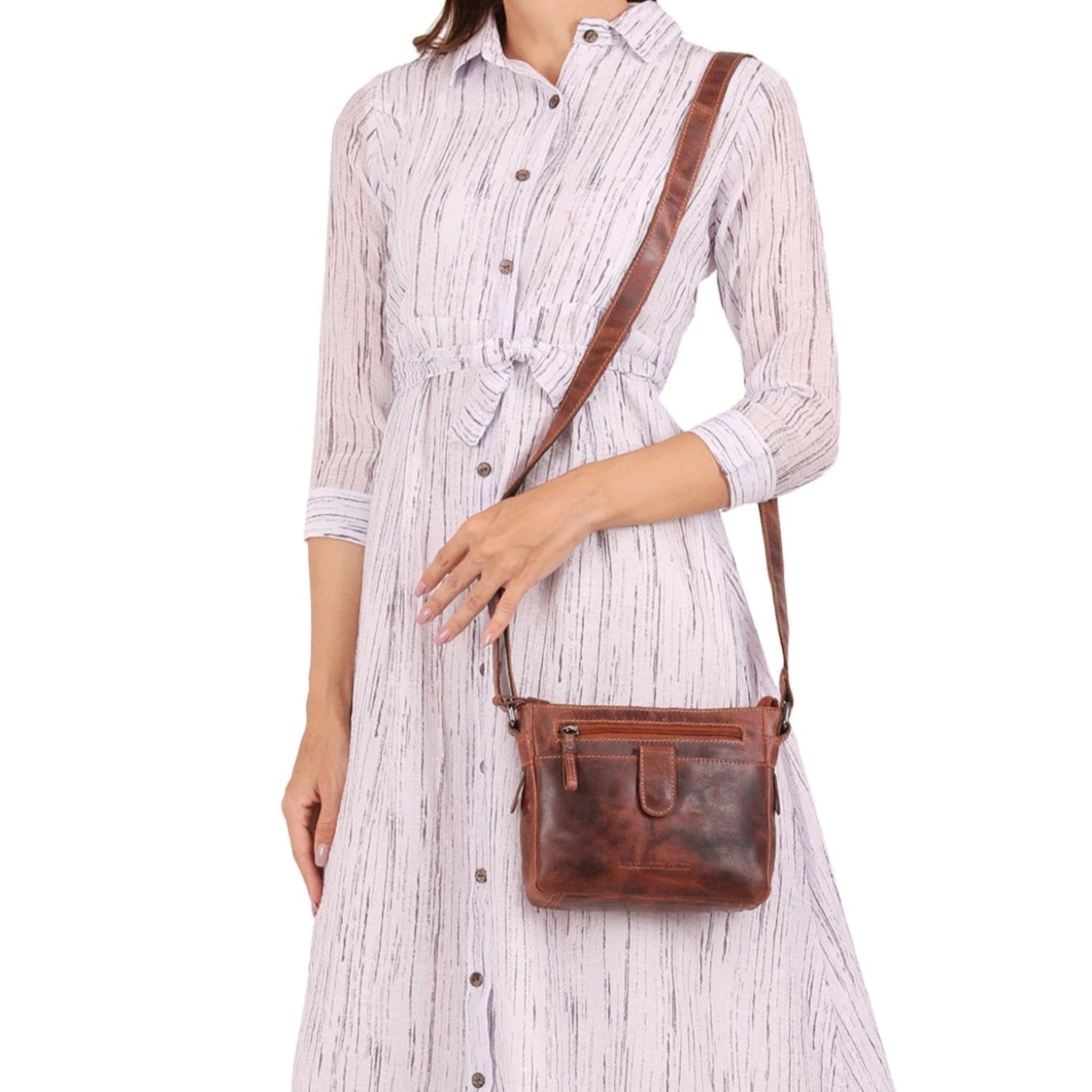 A woman wearing a white dress with a brown Minori leather crossbody bag on a white background