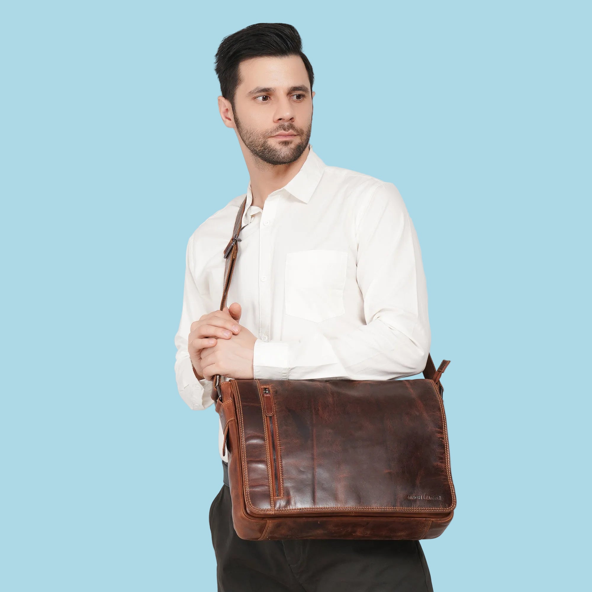 Man holding a brown leather bag against a plain background