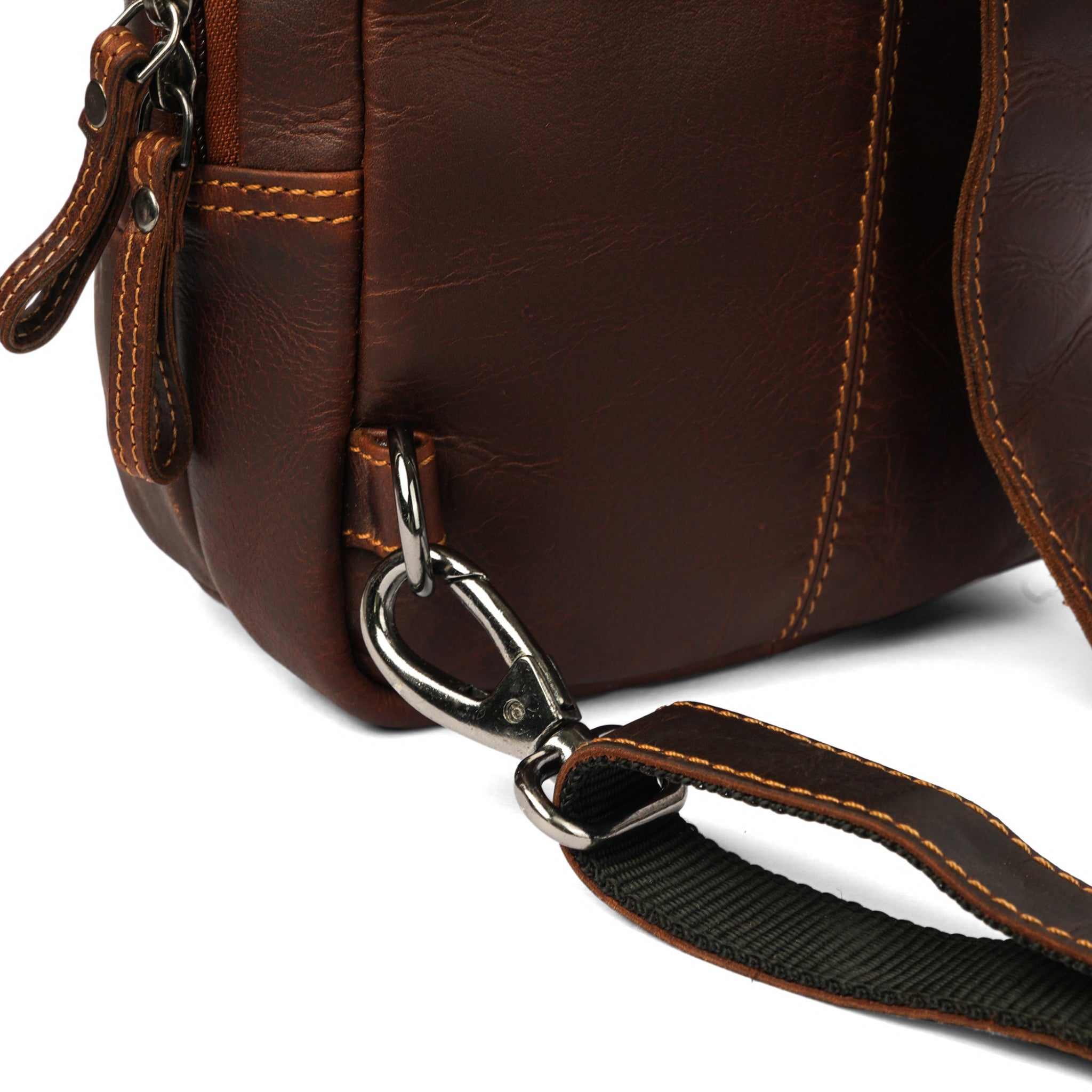 Close-up of the bottom corner of a brown Minori leather sling bag showing the metal clip and strap detail.