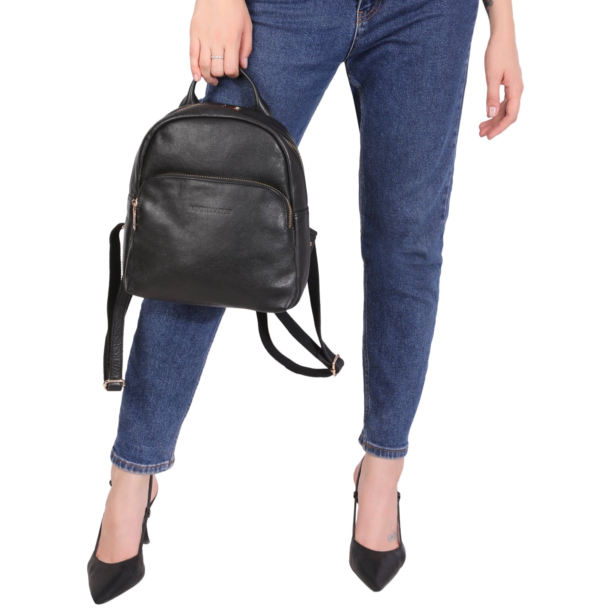Person wearing blue jeans and holding a black Minori leather backpack on a white background