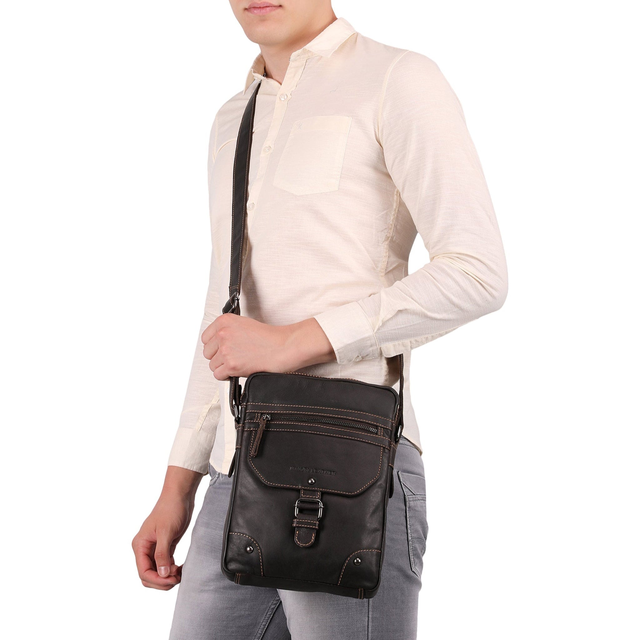 Man wearing a brown Minori leather crossbody bag with front buckle, zipper compartments, and contrast stitching.